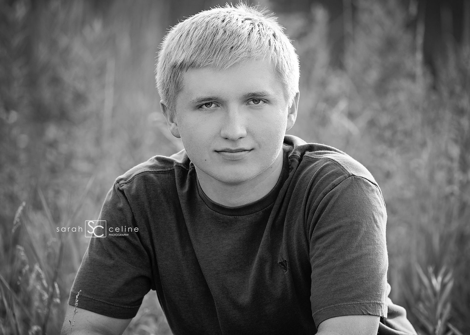 A black and white portrait photo of someone wearing a dark t-shirt sitting outdoors against a blurred natural background.