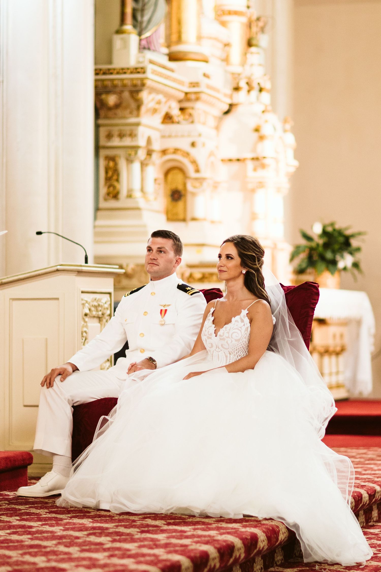Newlyweds relax on red carpet in an ornate church interior.