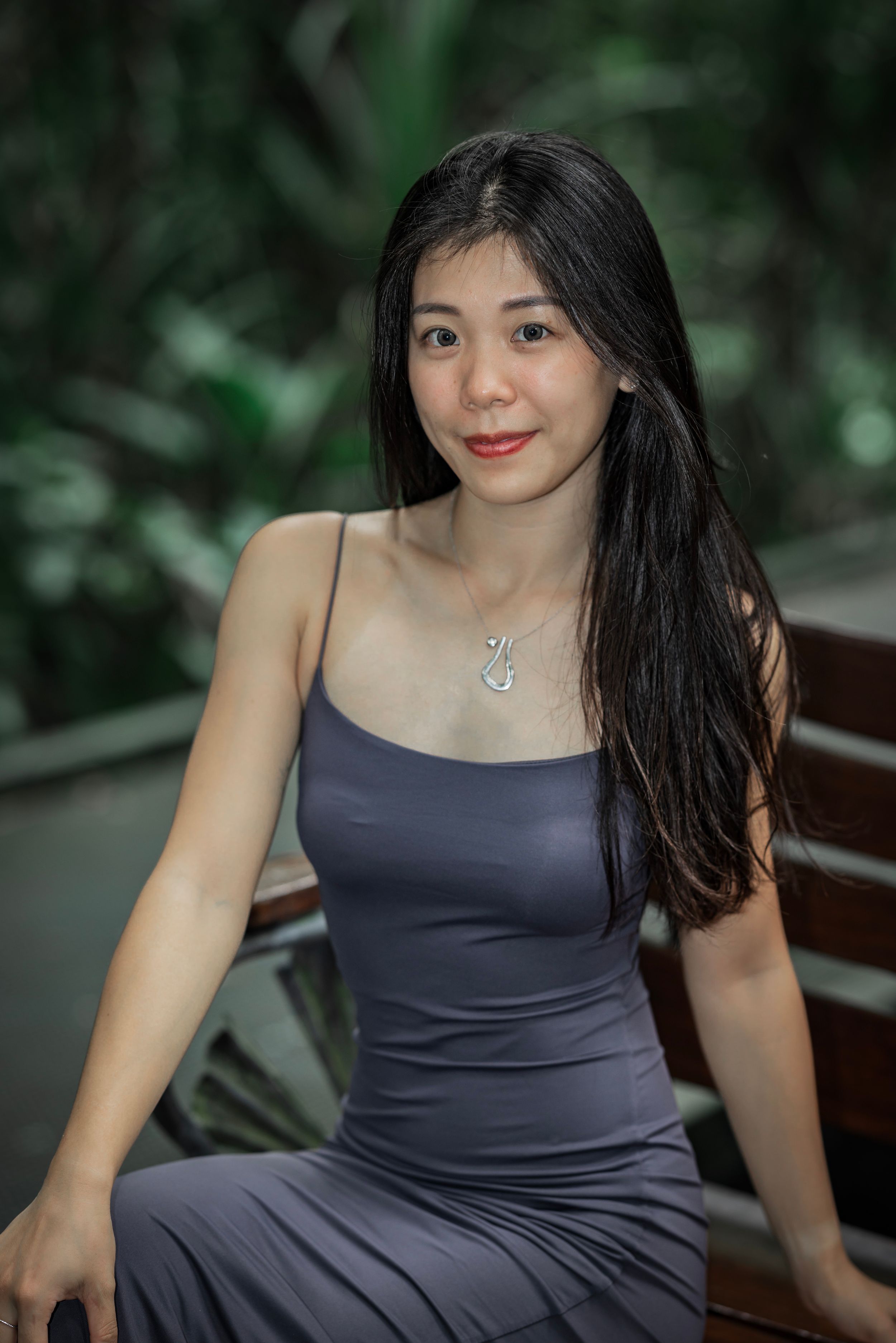 A person in a navy blue dress sits outdoors with lush greenery in the background.