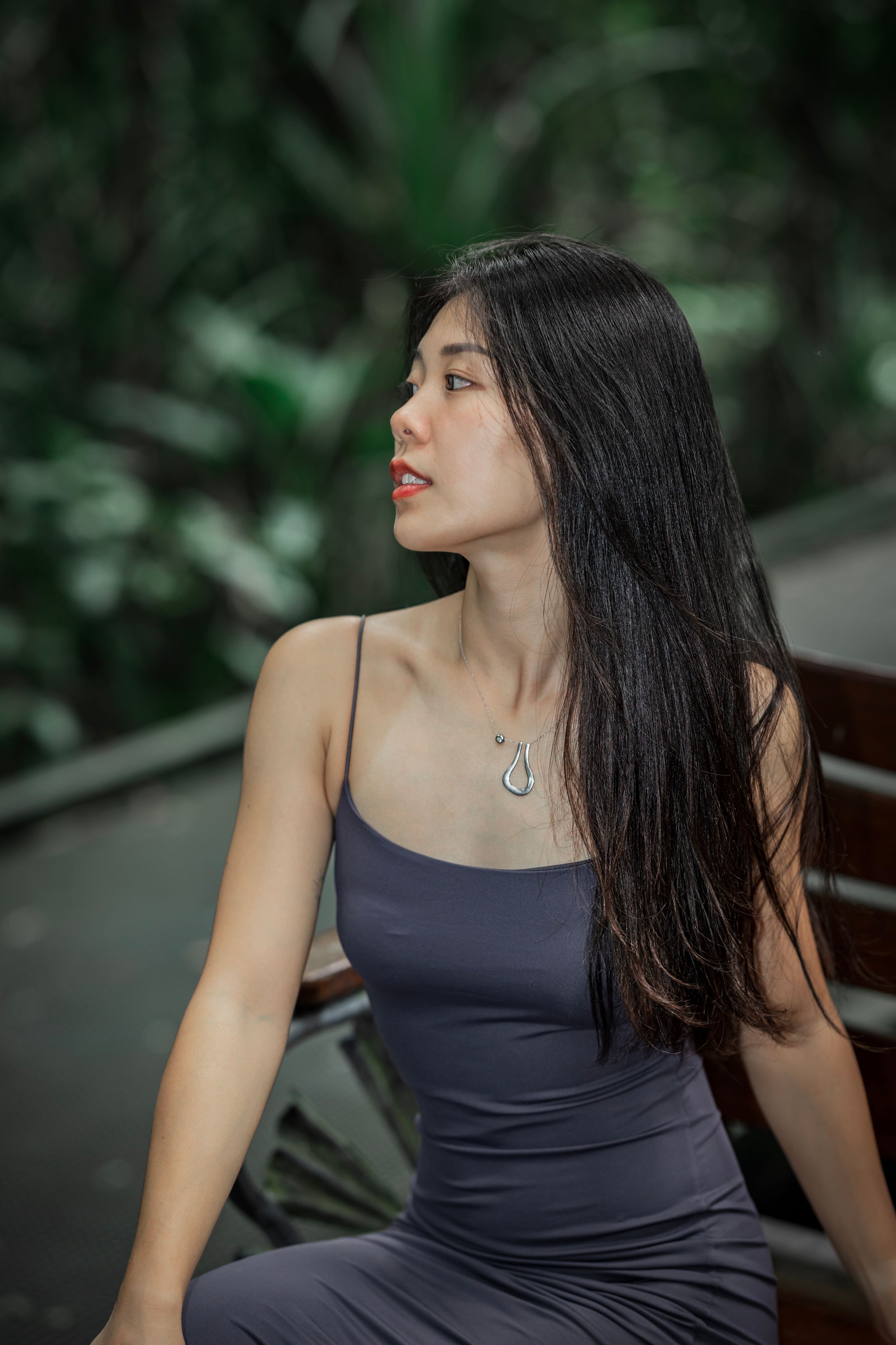 A set of photos showing someone in a navy blue sleeveless dress on a wooden bench with greenery in background.