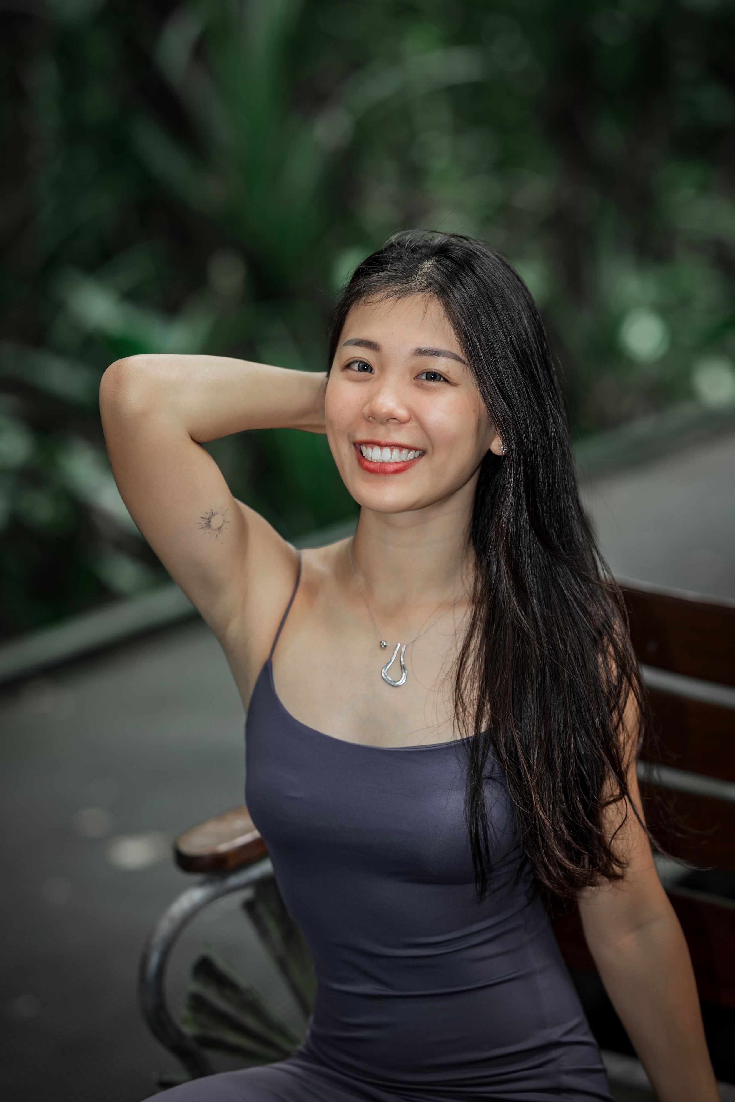 Woman in navy tank top laughs joyfully with windswept hair while posing against blurred natural background.