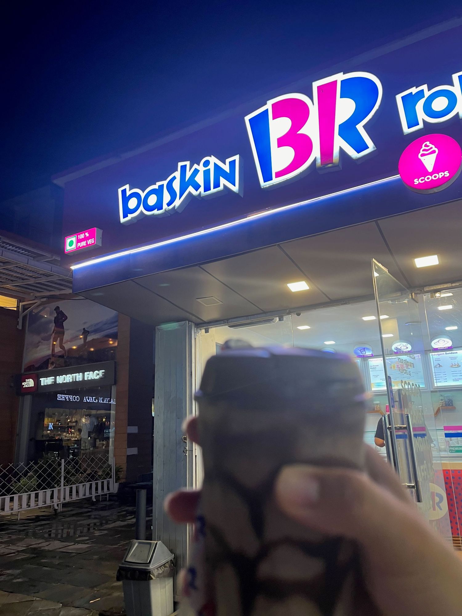 Illuminated Baskin Robbins storefront sign glowing in blue and pink neon at night.