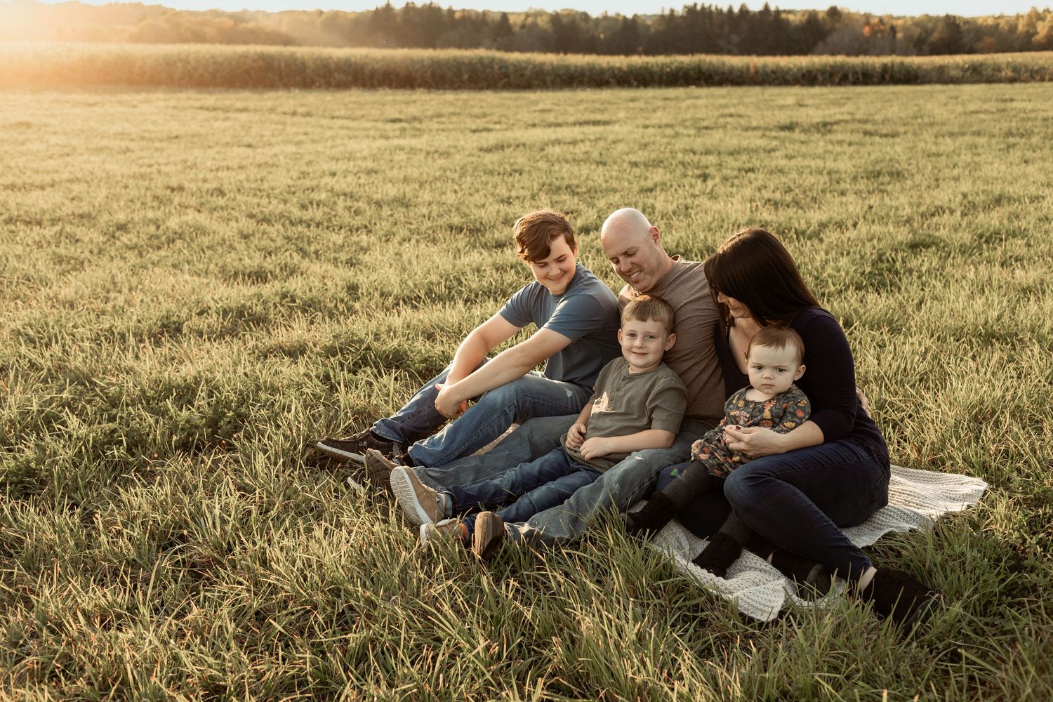 A joyful family sharing a tender moment together while sitting in a grassy field with dried plants on a sunny day.