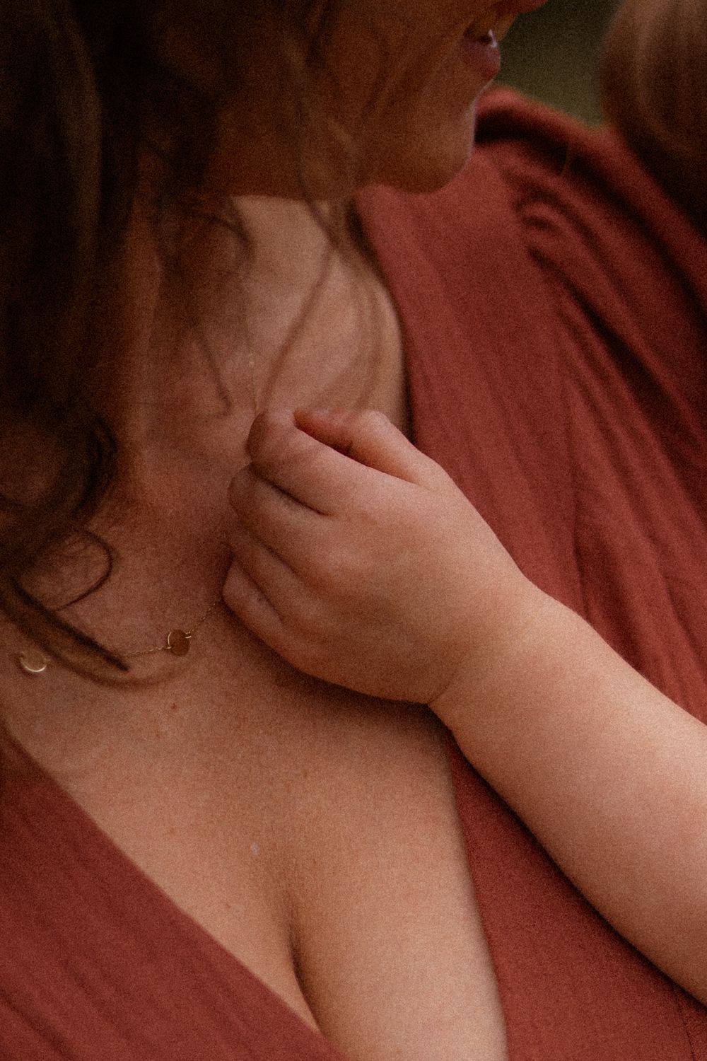Close-up artistic portrait showing bare shoulders and delicate hand gestures against a red backdrop in soft lighting.