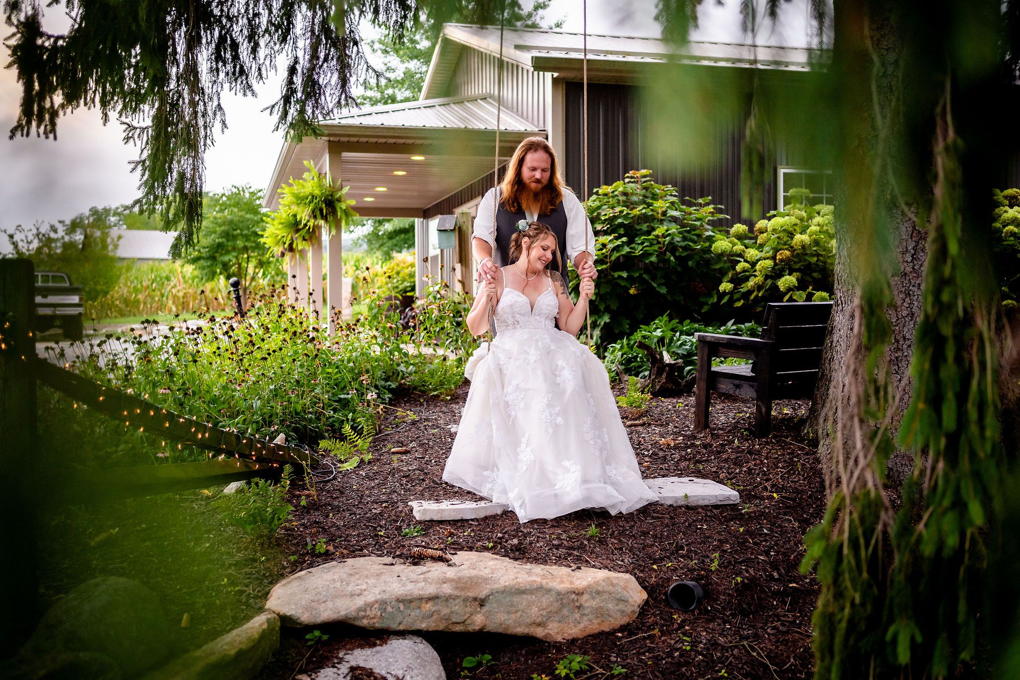 A couple poses for romantic portraits under drooping willow trees in a garden setting.