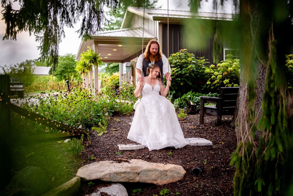 A couple poses for romantic portraits under drooping willow trees in a garden setting.