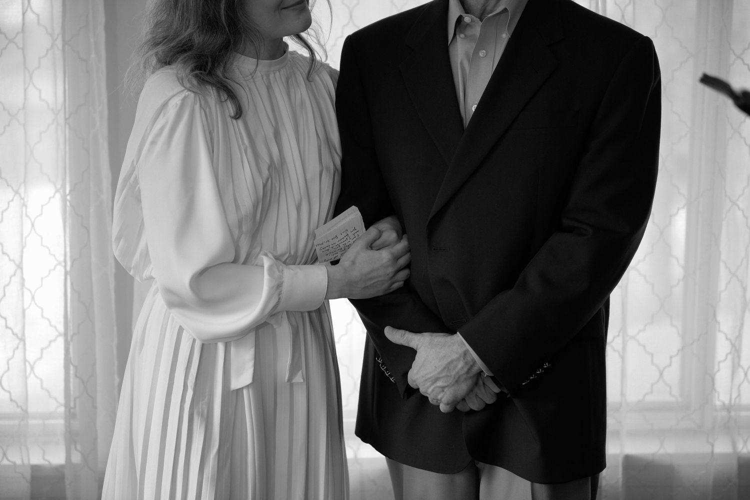 A bride and groom stand side by side embracing at their small intimate ceremony indoors.