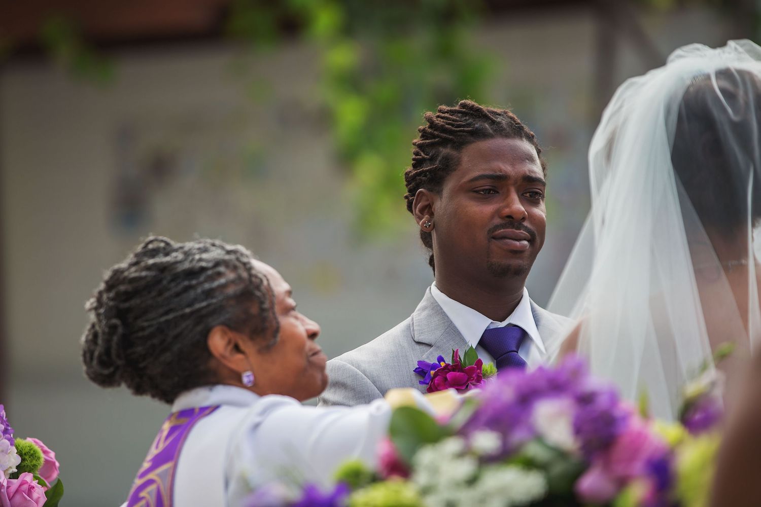 Wedding ceremony guests gather outdoors with purple floral decorations.