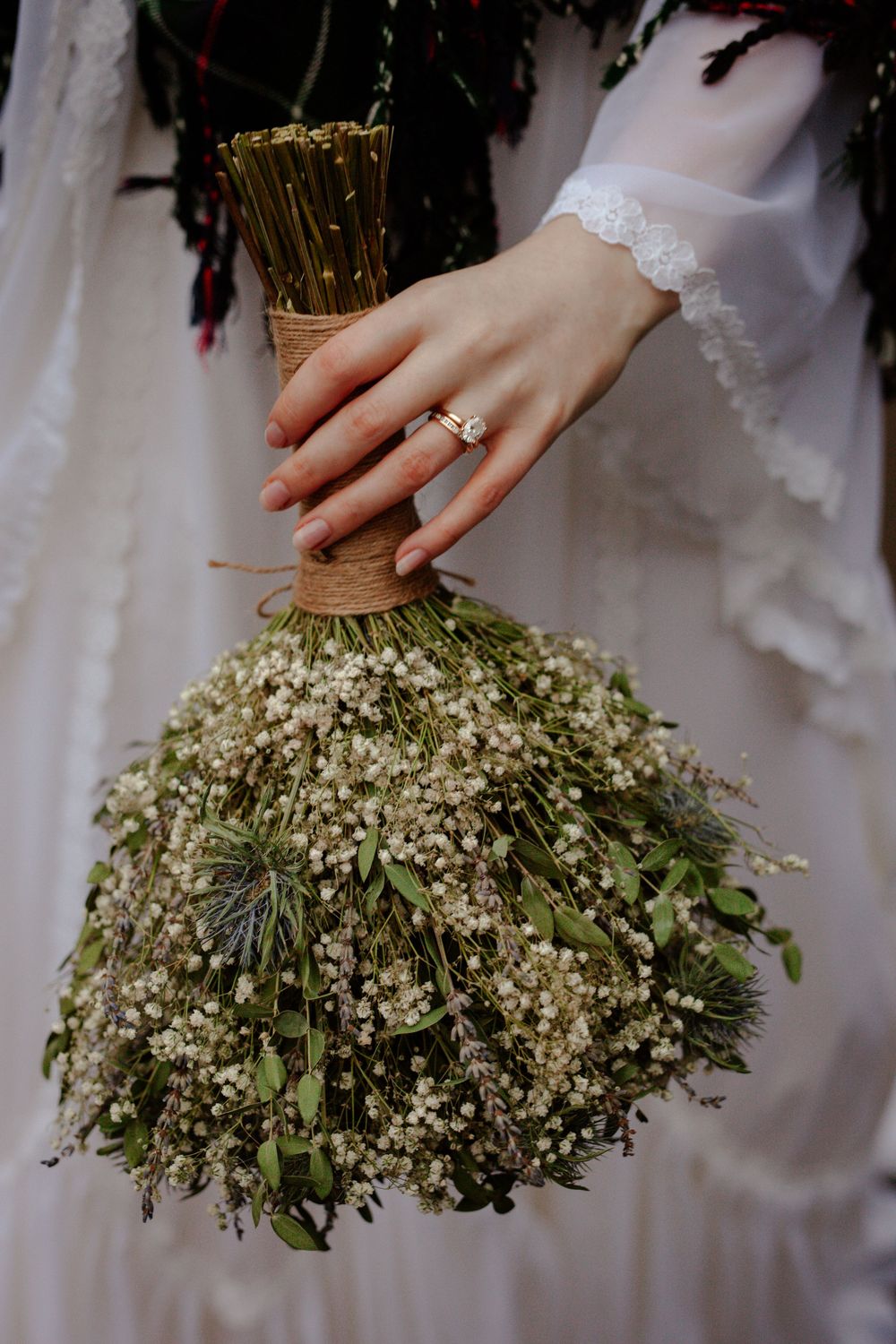 A delicate lace-cuffed hand holds a rustic bouquet of baby's breath flowers tied with twine.