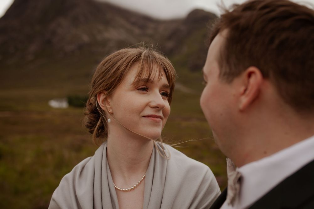 A couple shares a tender moment against the dramatic backdrop of Scottish highlands.