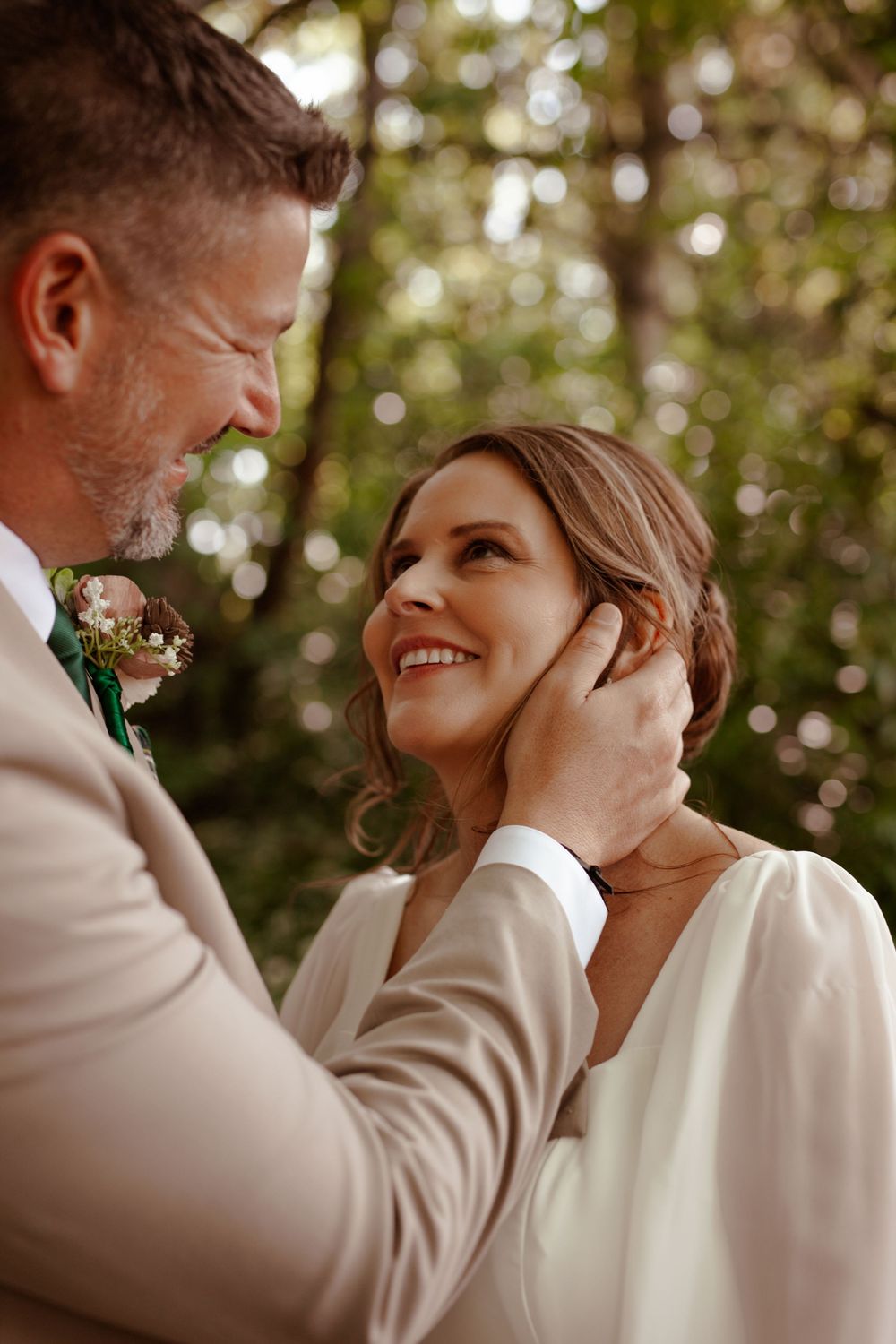An intimate wedding moment captured in warm sunlight beneath forest trees.