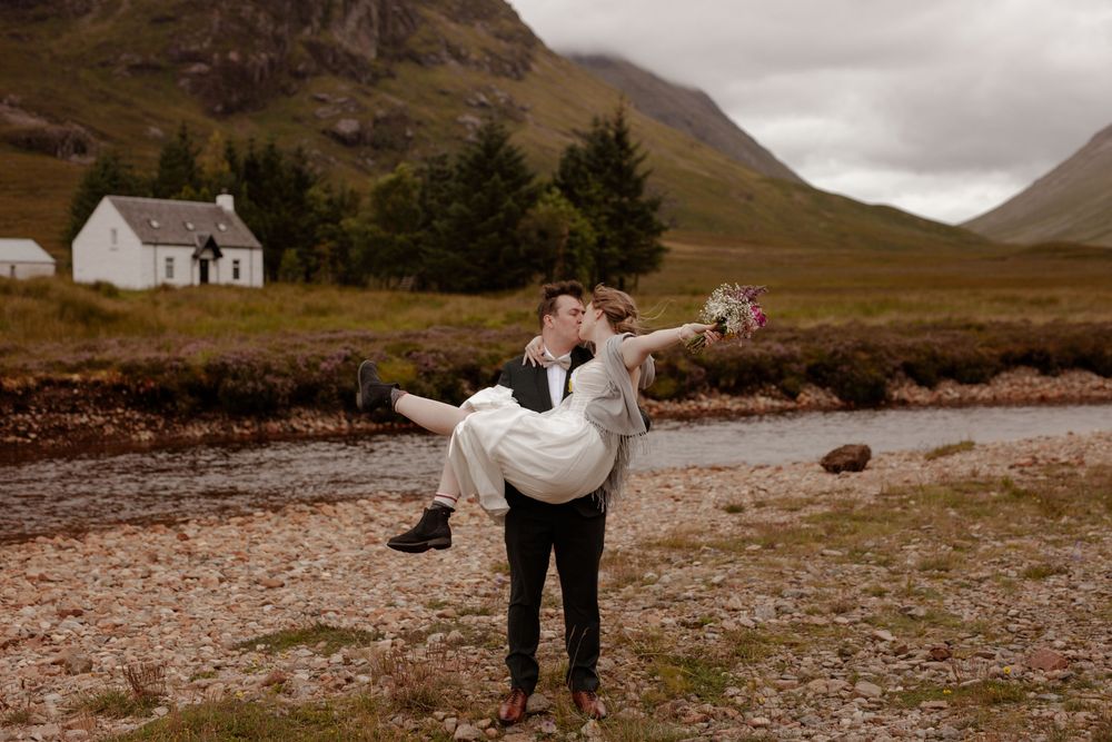 A romantic lift pose near a white cottage in the misty Scottish highlands.