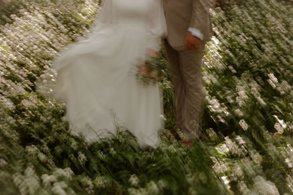 An artistic wedding photo showing dress and suit details among blooming flowers.