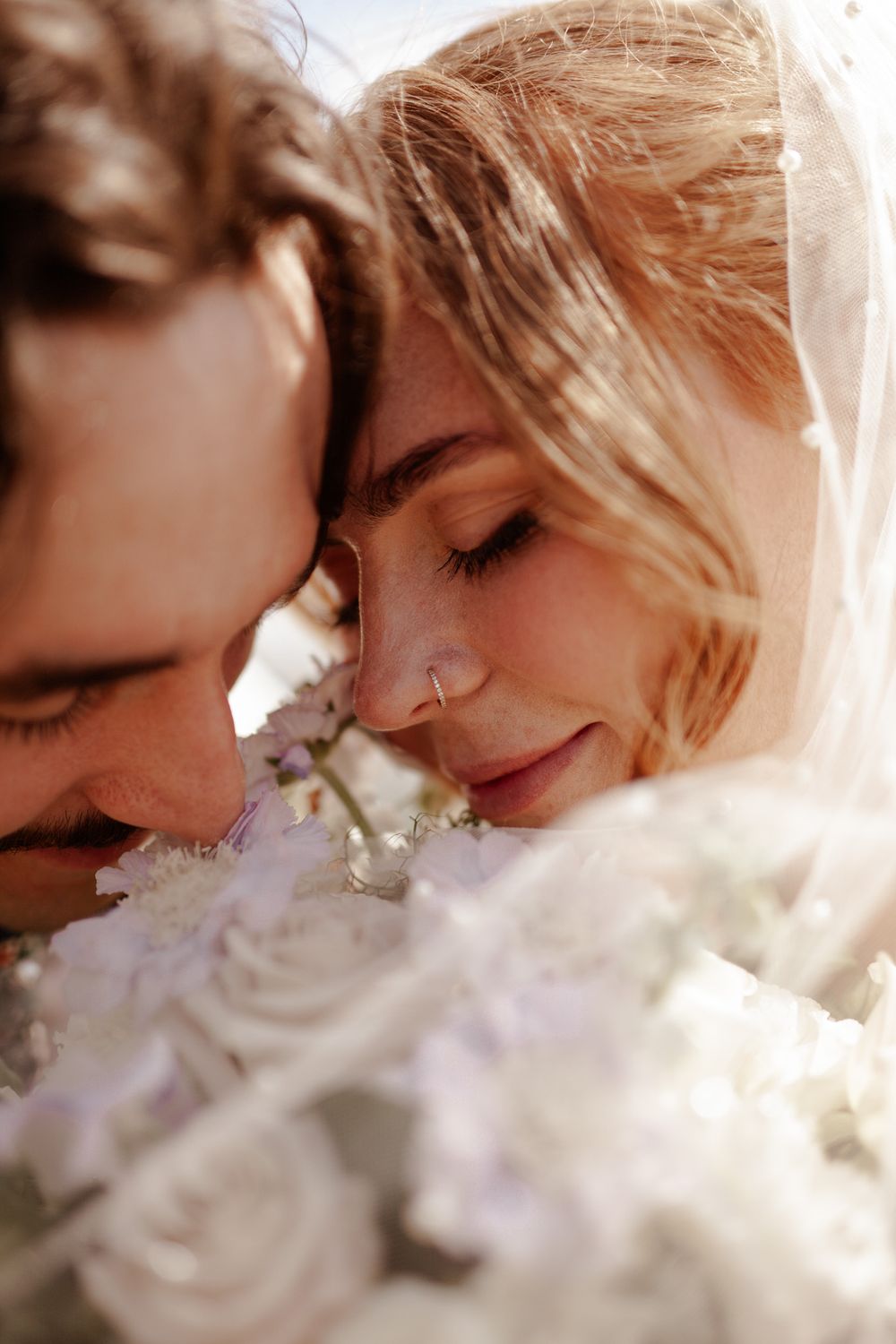 A romantic close-up moment between newlyweds with white roses in soft lighting.