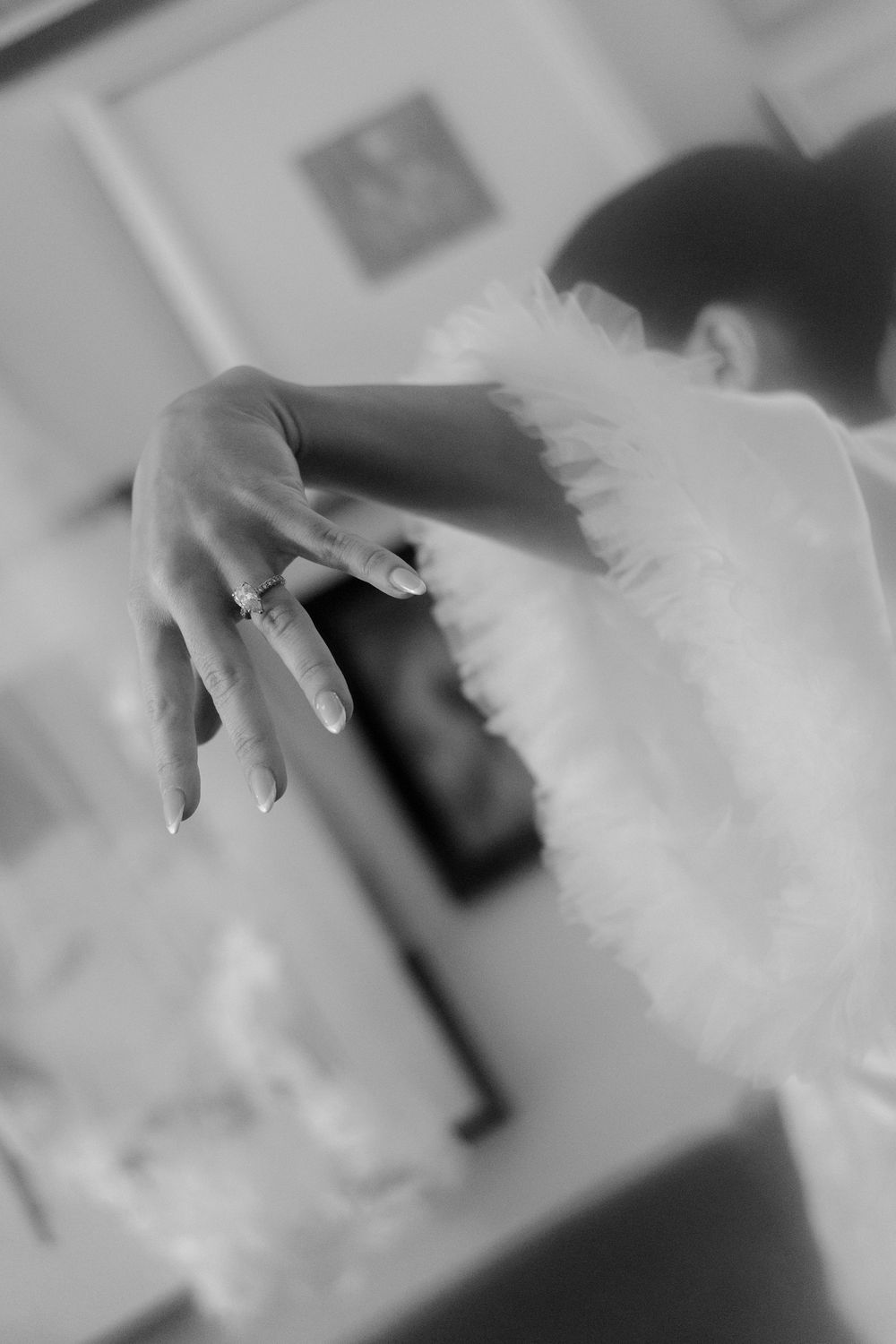 Close-up black and white photo of an elegant hand with engagement ring and feathery details.