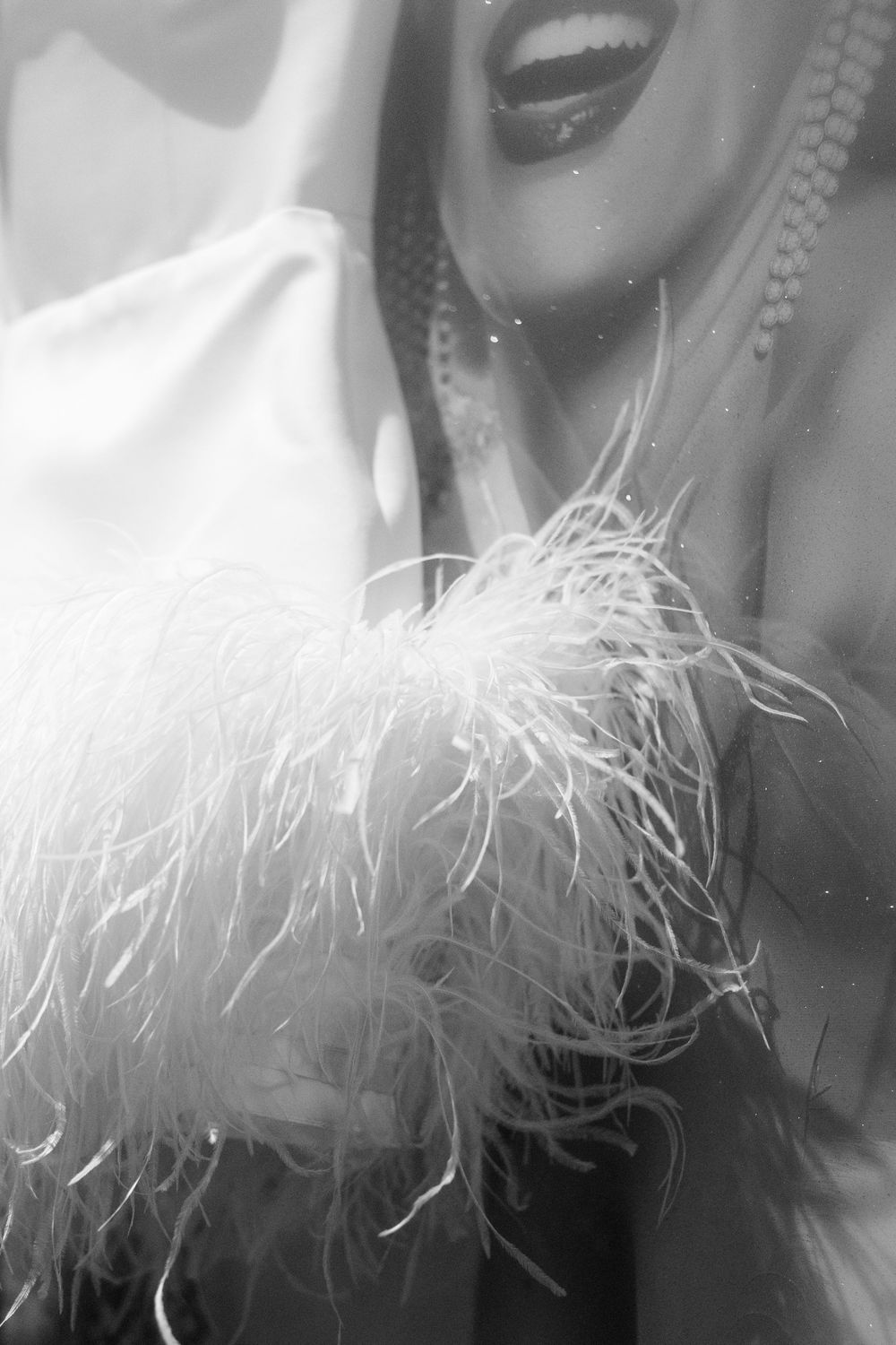 Close-up black and white photo of white feathers and fabric with pearl necklace details.