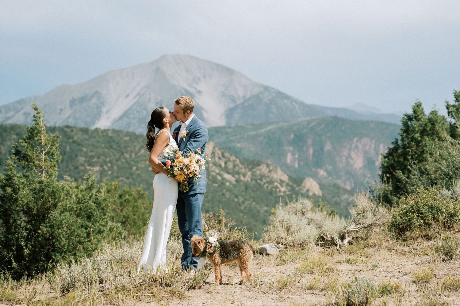A couple celebrates their wedding day on a mountaintop with their small dog and a beautiful floral bouquet. Elopement Photography in Aspen.