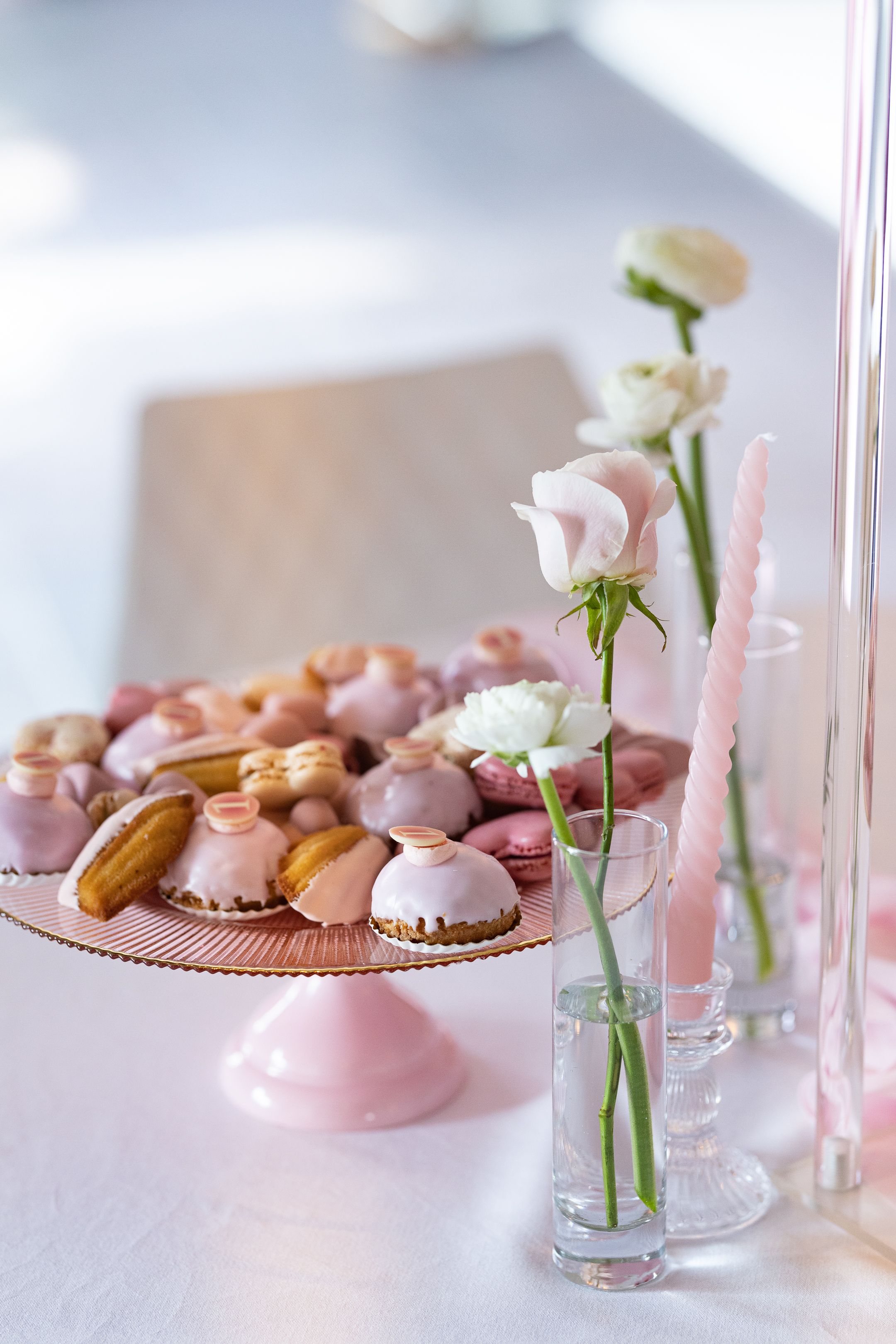 Pink macarons and delicate flowers in glass vases arranged on white tablecloth.