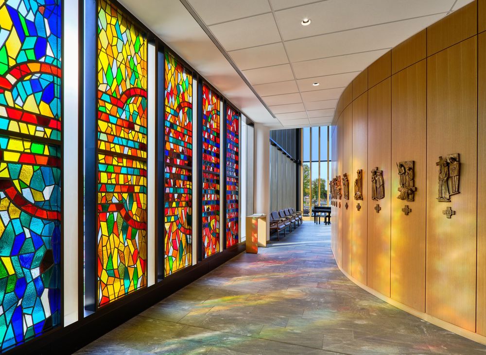 A curved hallway features colorful stained glass windows alongside wooden paneled walls in a modern architectural setting.