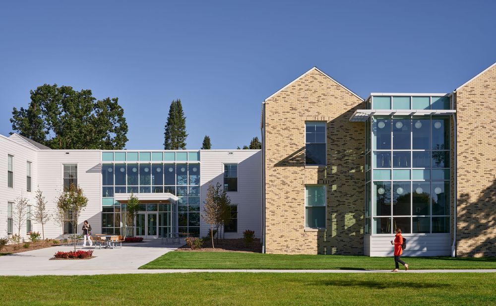 Modern campus building with tan stone walls, glass windows and green lawn on a sunny day.