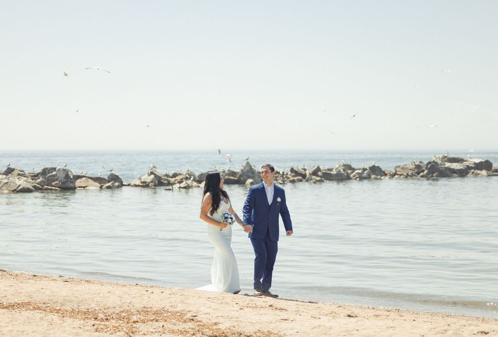 A couple walks together along a peaceful rocky beach shoreline on a bright summer day.