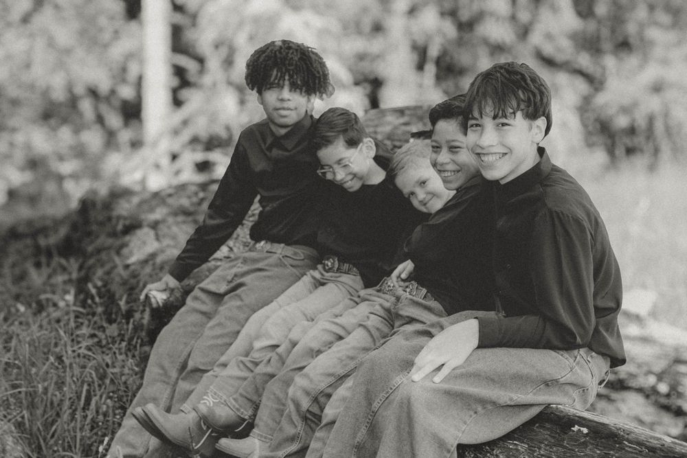 Vintage black and white photo of four young children sitting together on a log outdoors.