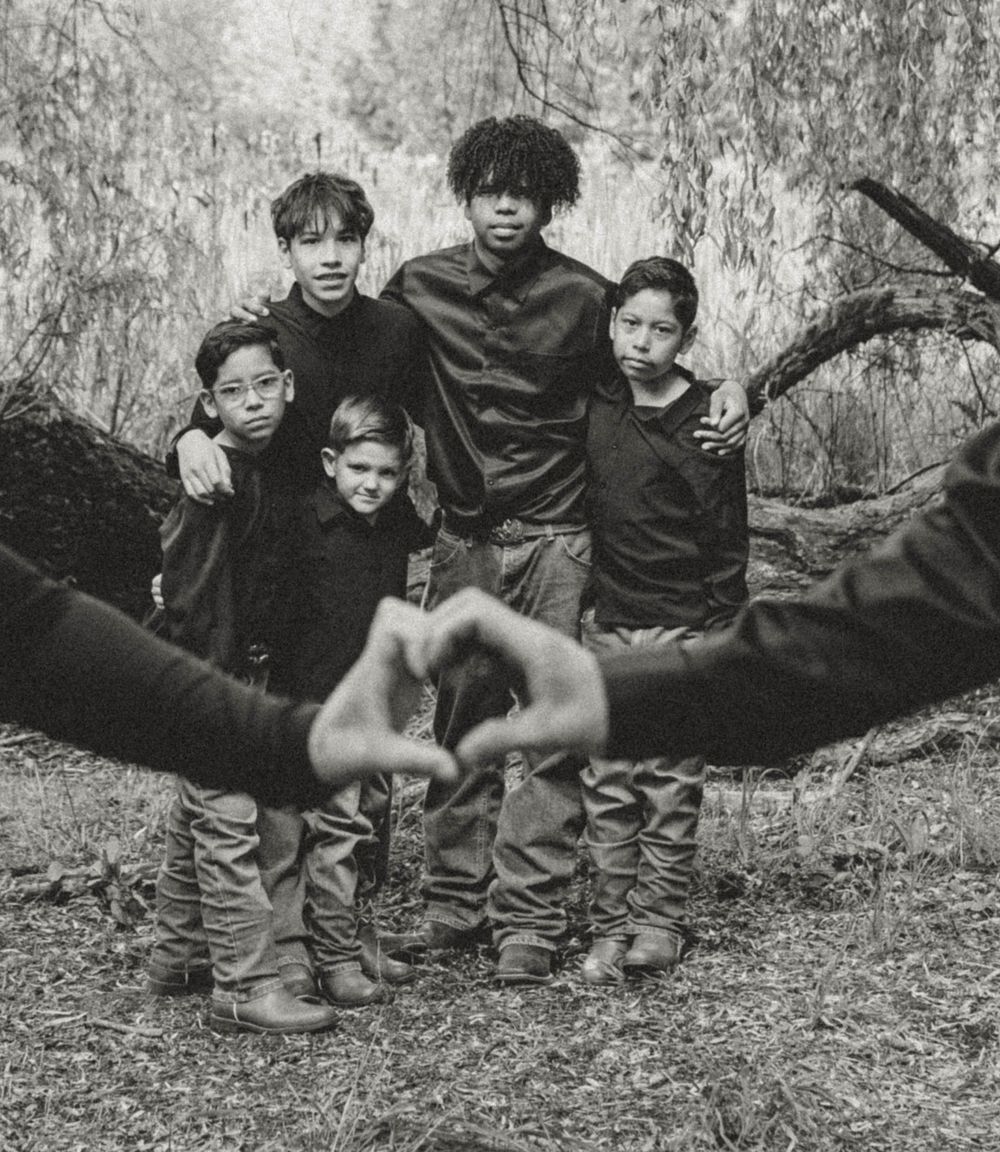Black and white photo of five children posing together outdoors with heart hand gesture in foreground.