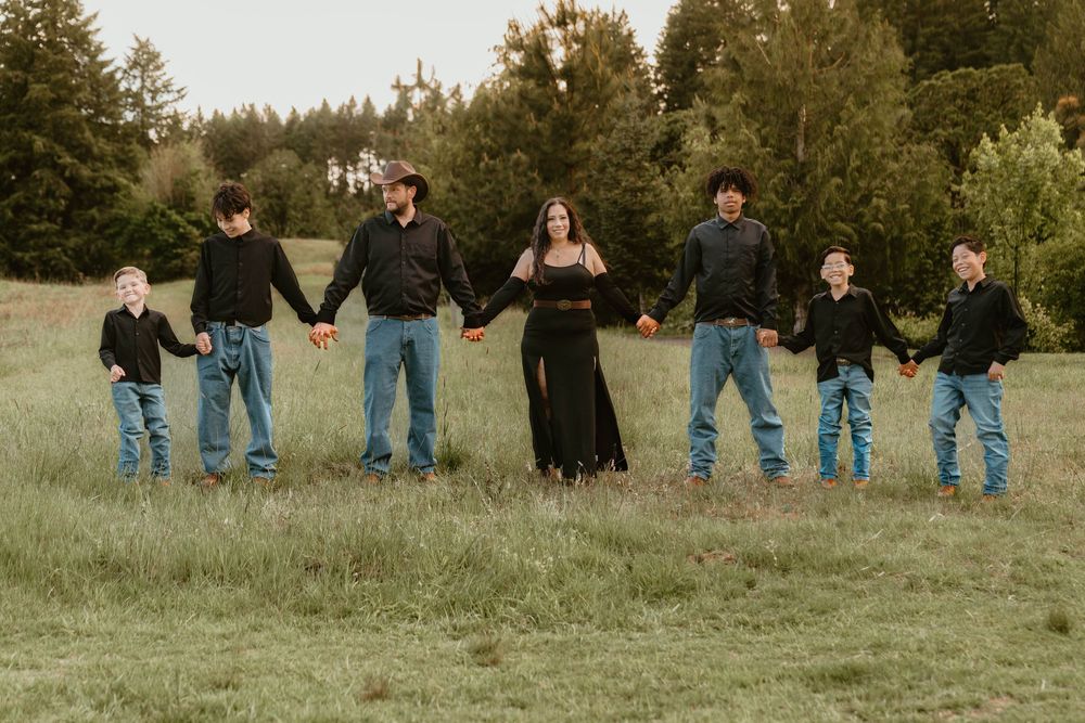 Large family of seven holding hands in a green field at sunset wearing coordinated black and denim.