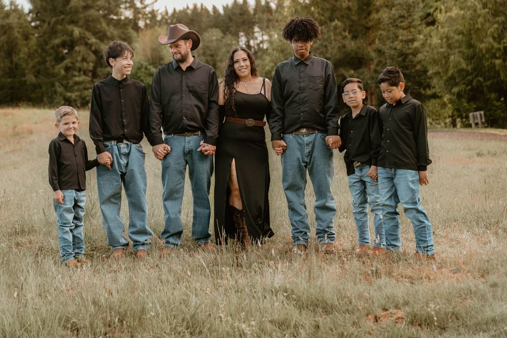 Family of seven posing in a field wearing matching black tops and jeans.