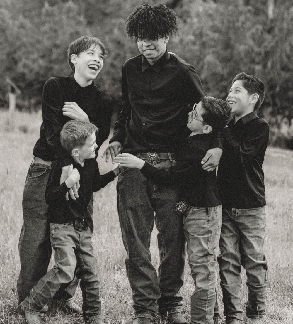 Five boys laughing and playing together in a grassy field in black and white.