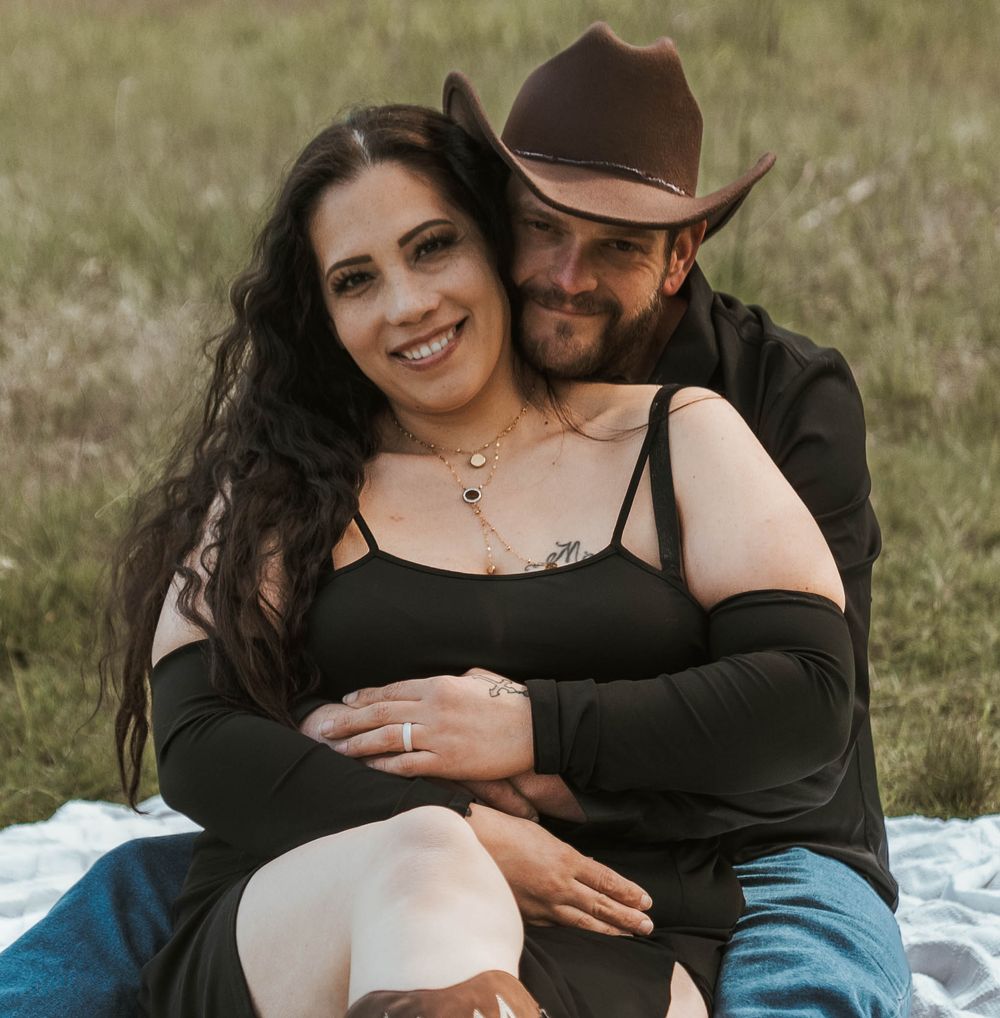 Couple smiling and embracing on a blanket in a sunny field.