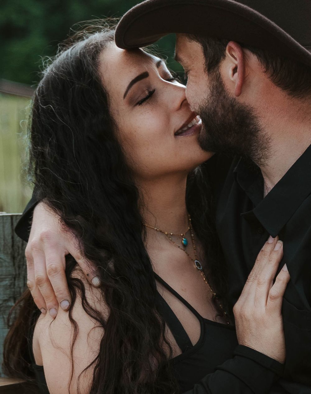 Romantic couple sharing a tender moment outdoors, man wearing a cowboy hat.