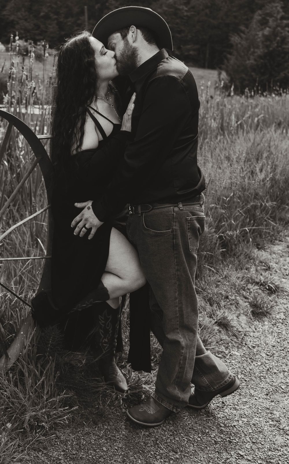 Couple sharing a passionate kiss near a vintage wagon wheel in black and white.