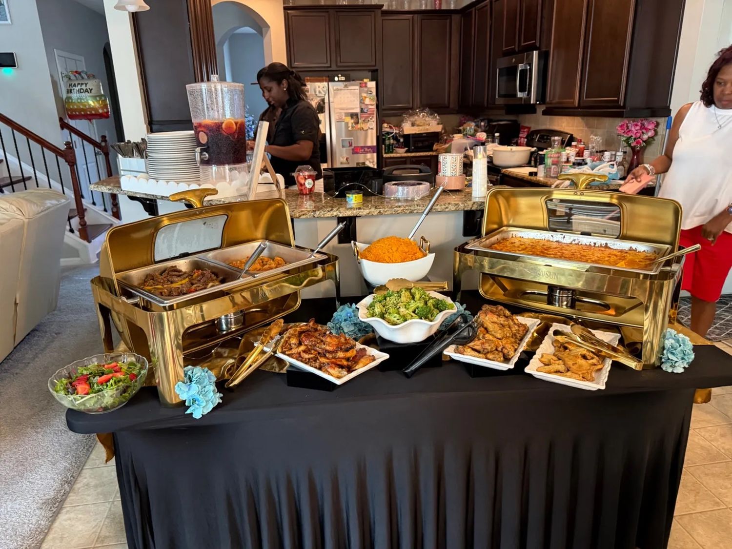 Elegant catering buffet setup with multiple chafing dishes and appetizers displayed on a black tablecloth.