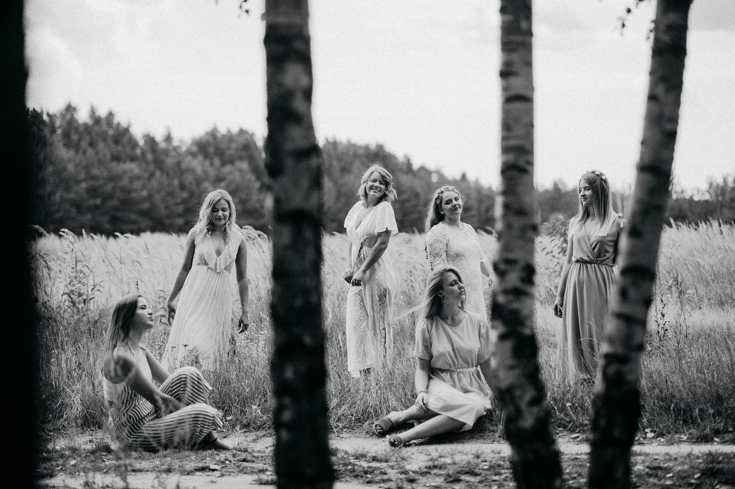 A black and white photo of people in white dresses gathered among birch trees in a field.