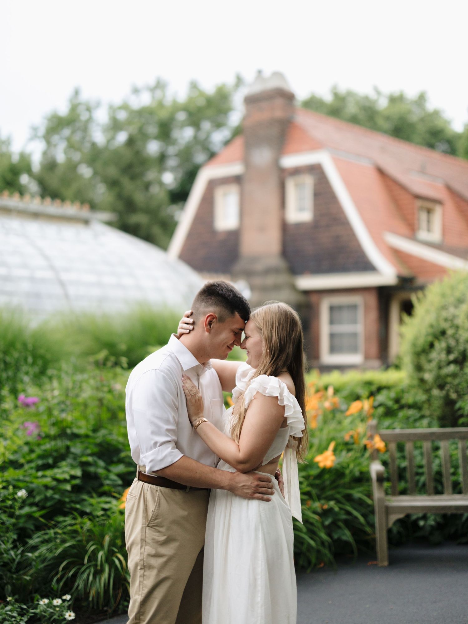 A romantic moment shared in a garden with lush flowers and a charming cottage house in the background.