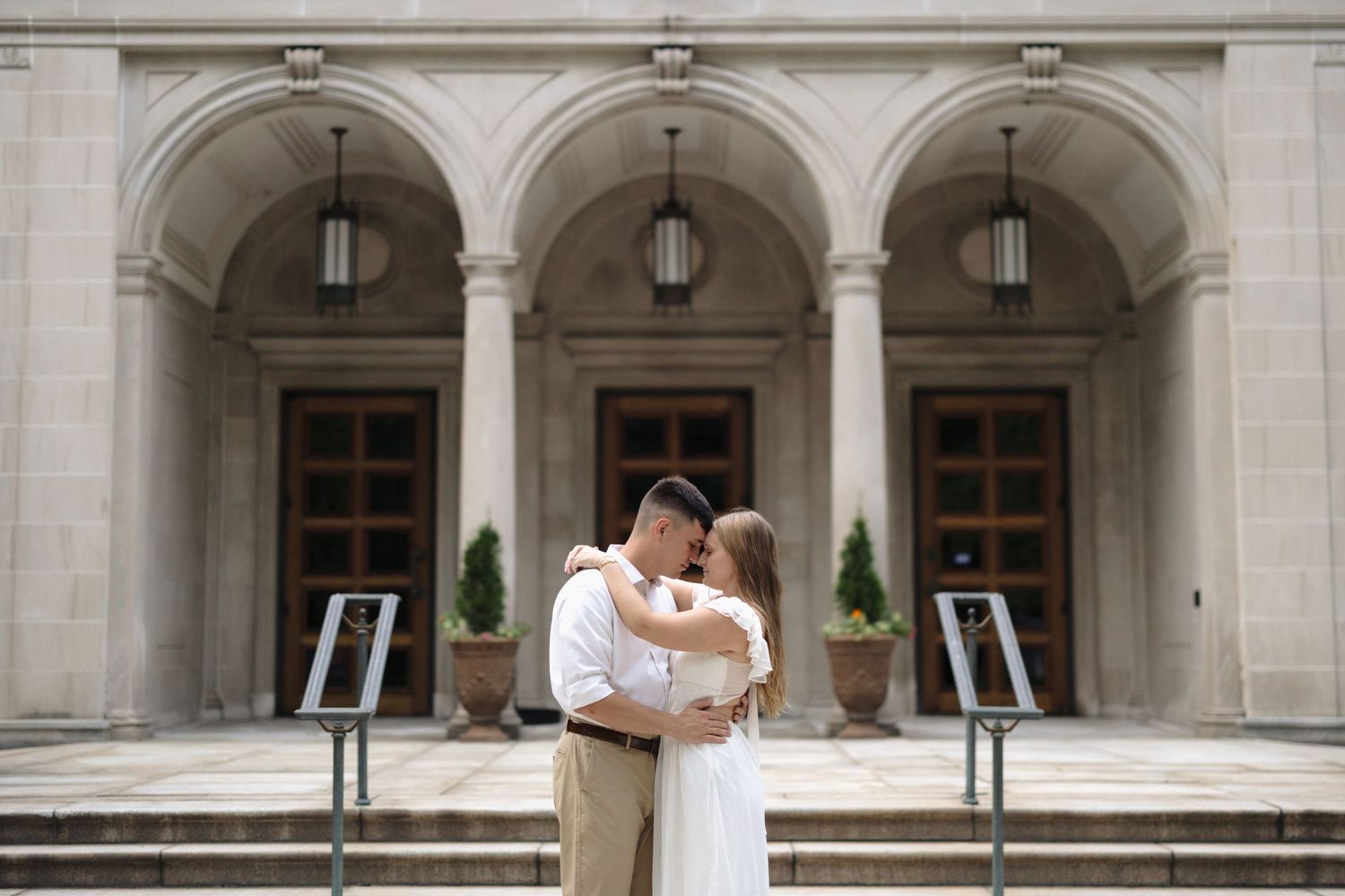 A couple embraces in a tender moment outside a grand building with stone archways and hanging lanterns.