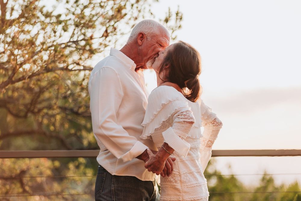 A loving couple embraces during golden sunset hour on an outdoor deck with autumn trees in background.
