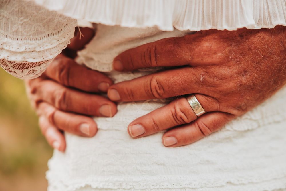 Close-up of hands with a gold wedding ring against white fabric during a wedding ceremony.