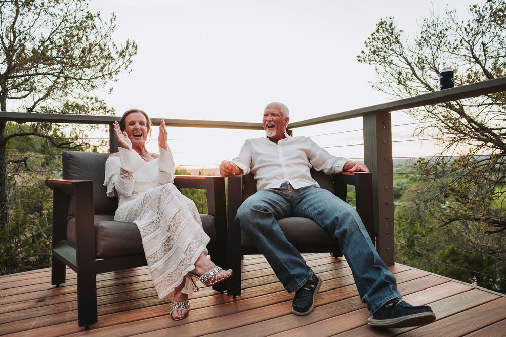 People lounging and laughing together on a wooden deck overlooking a scenic wooded landscape at sunset.