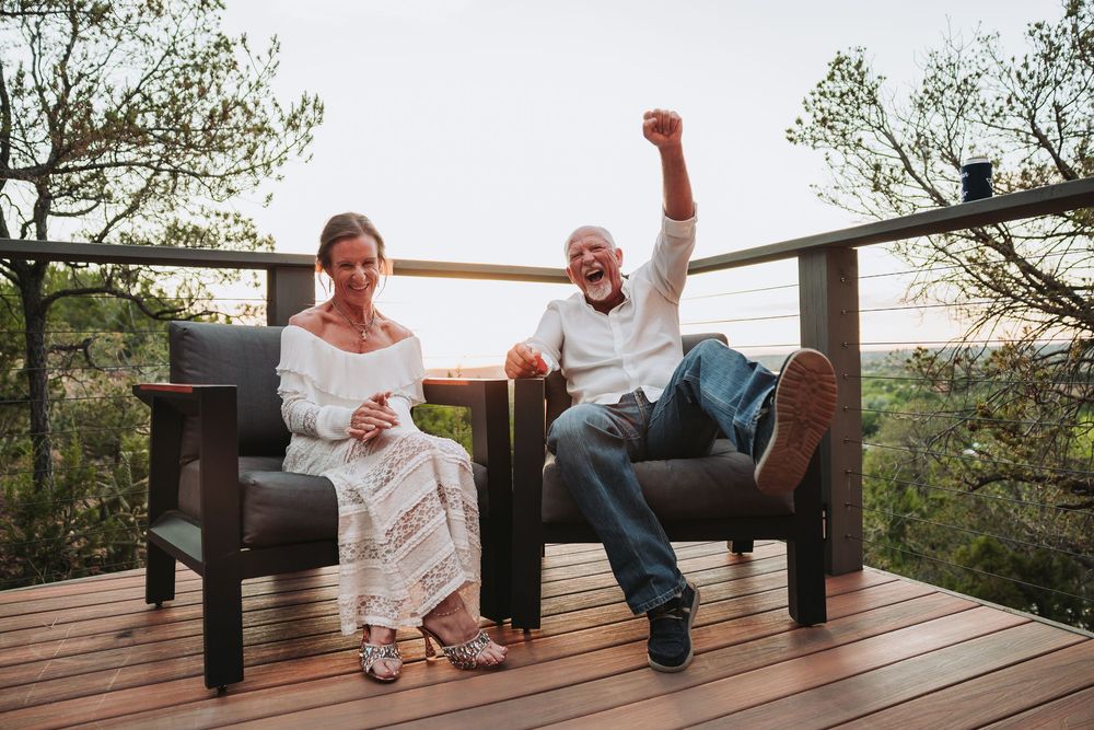 Two people sharing a laugh while sitting together on a rustic wooden deck at sunset.