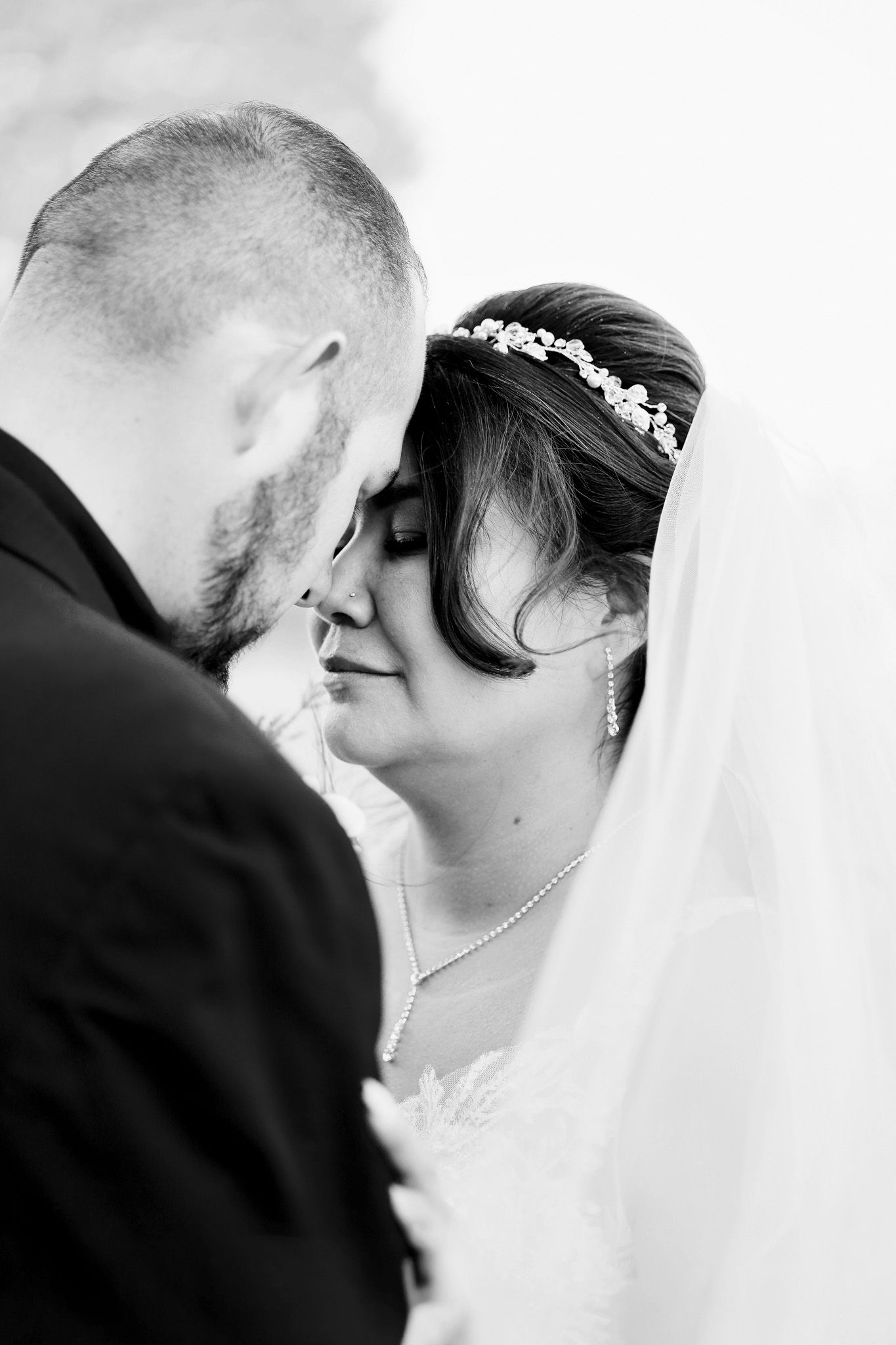 A wedding couple stands together under a white archway at an outdoor venue while holding a floral bouquet.
