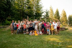 Large group photo of wedding guests gathered on a grassy hillside during sunset.