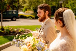 A wedding couple walks along a garden path surrounded by lush landscaping and natural light.
