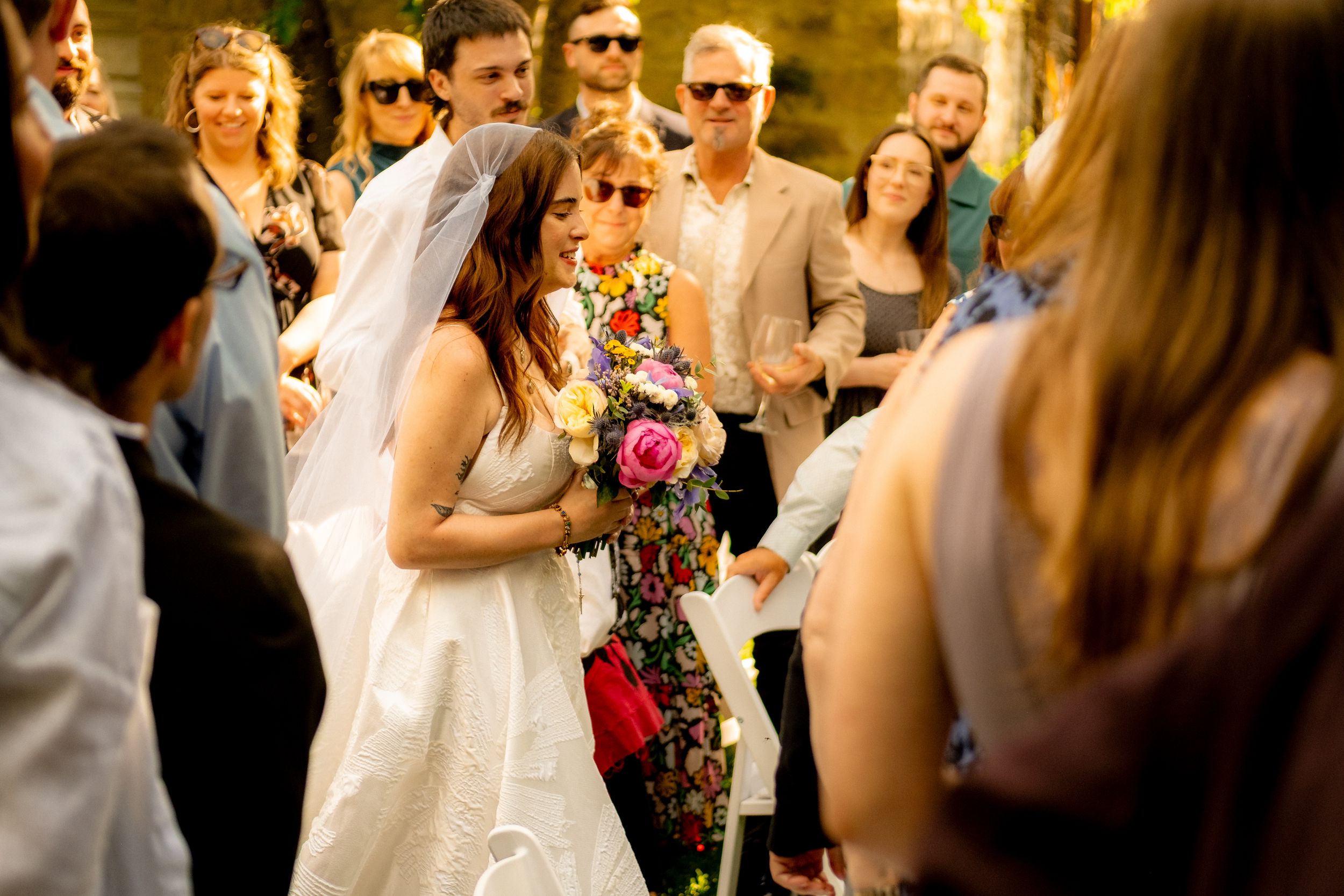 Bride in white dress celebrates with wedding guests during outdoor reception.