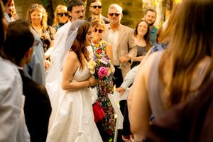 Bride in white dress celebrates with wedding guests during outdoor reception.