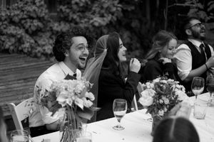 Wedding guest laughs joyfully at reception table with floral centerpiece.