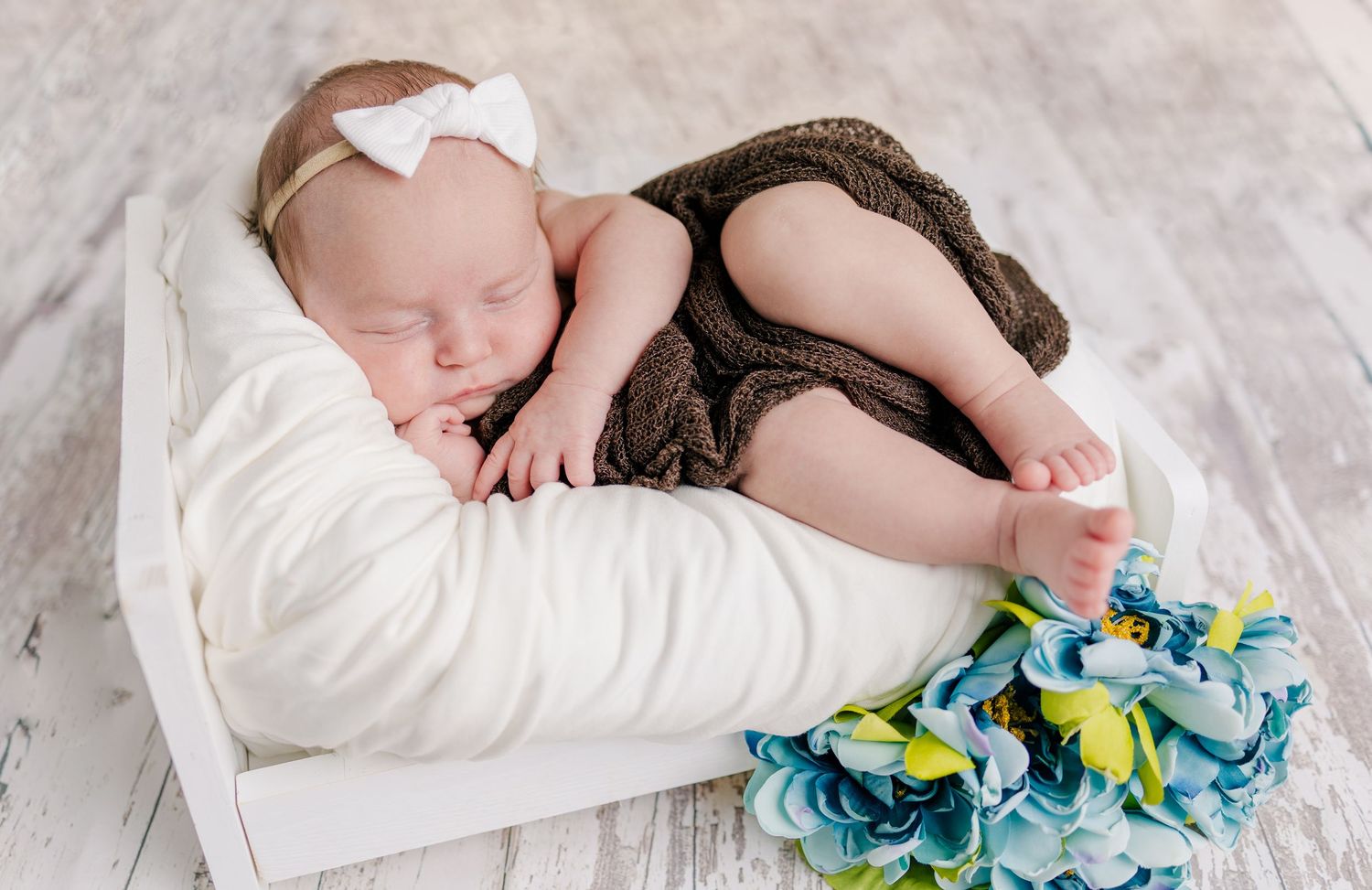 A newborn baby sleeping peacefully in a gray woven basket on a light-colored background.