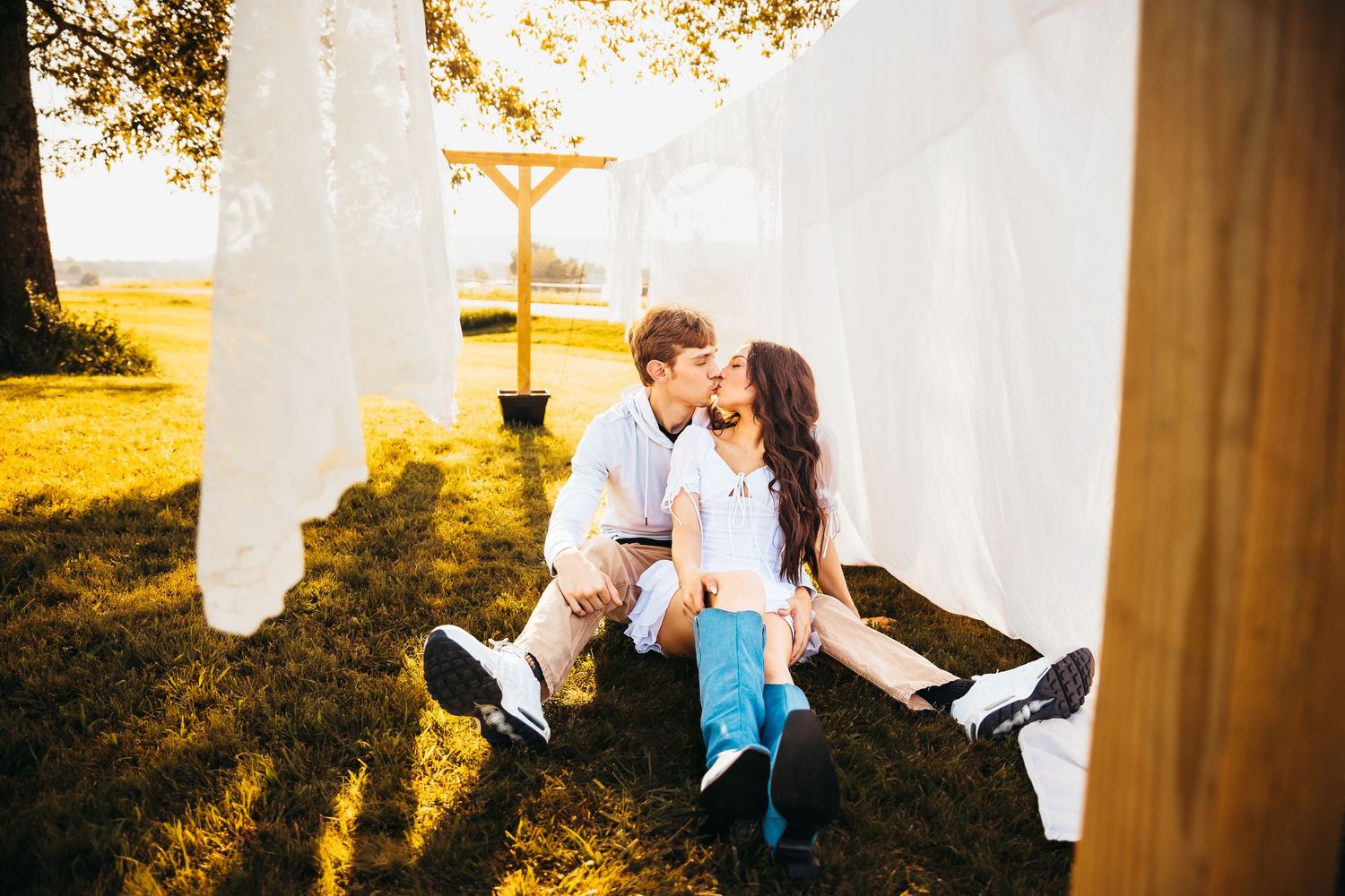 Couple sitting among white flowing fabrics during golden hour outdoor photoshoot.