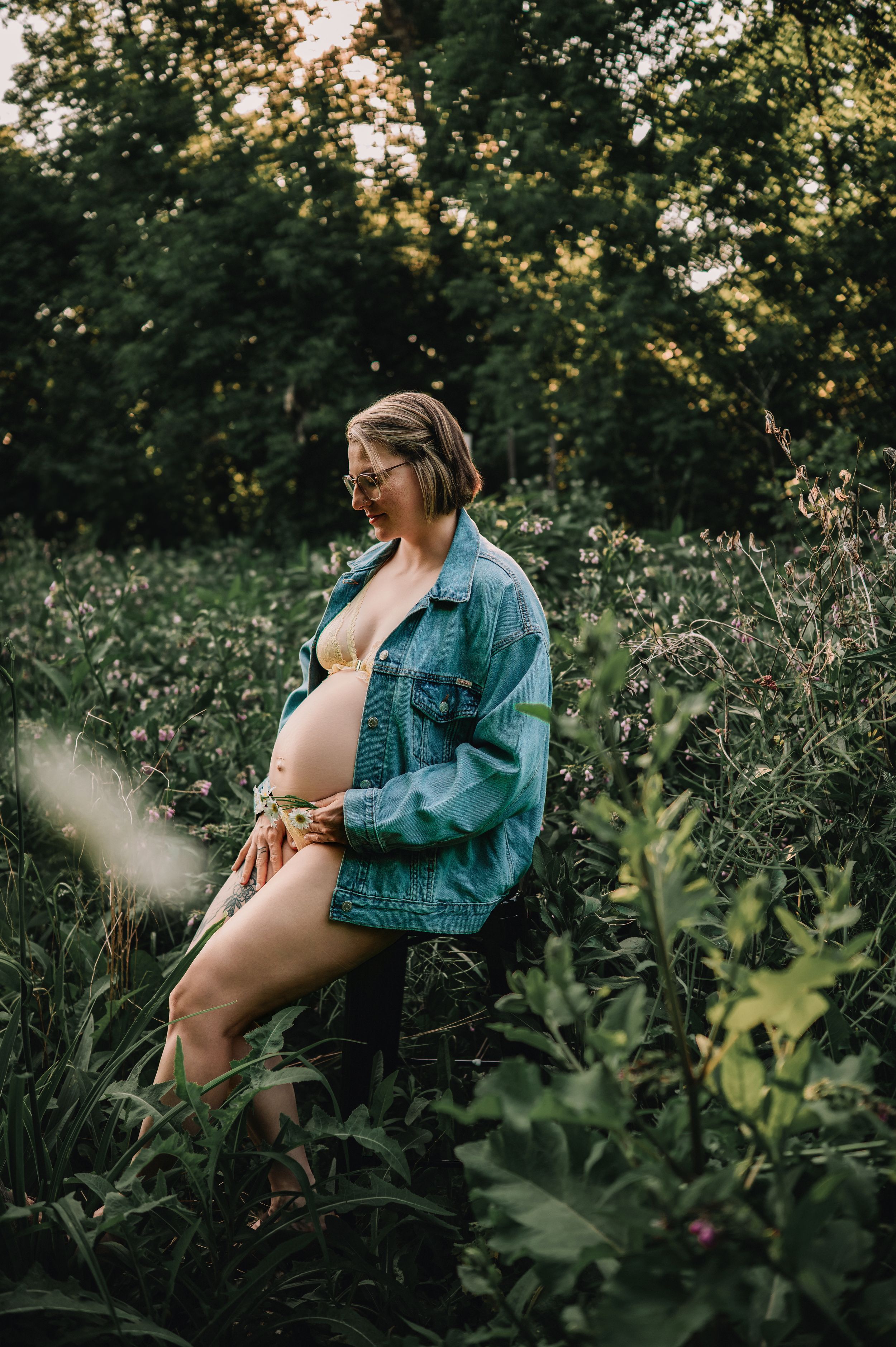 A dreamy outdoor maternity photo in tall grass and wildflowers during golden hour lighting.